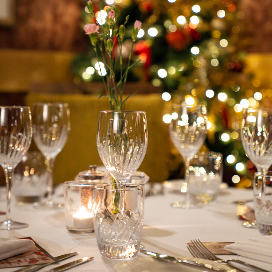 Crystal glassware and candlelight on a table in the ristorante, Christmas lights glowing behind