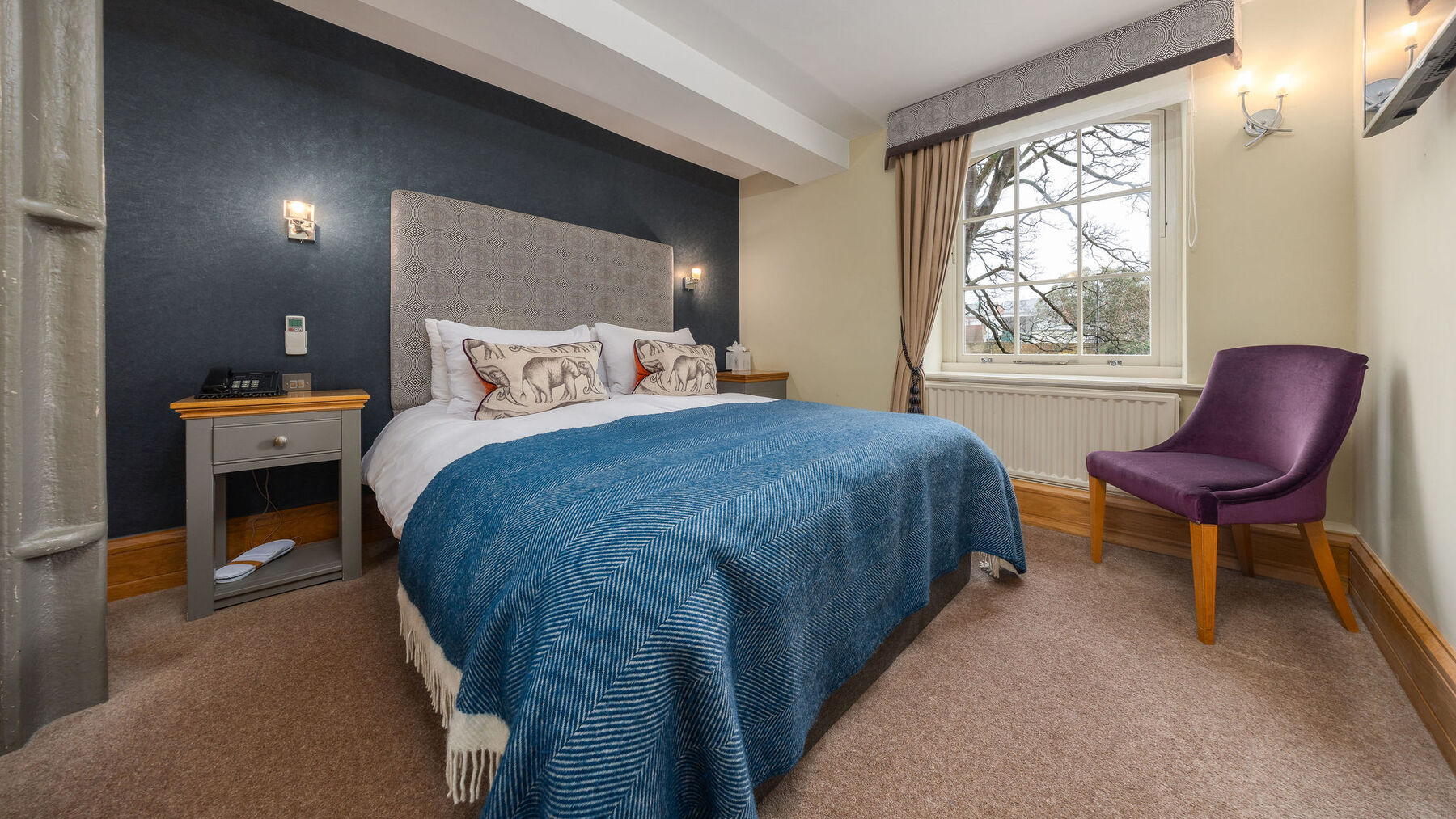 A boutique guest room at Ennios, with a made bed and armchair by the window